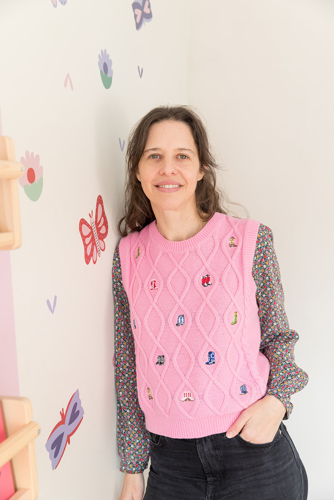 Founder wearing a pink knitted vest with embroidered characters against a wall with butterfly decals.