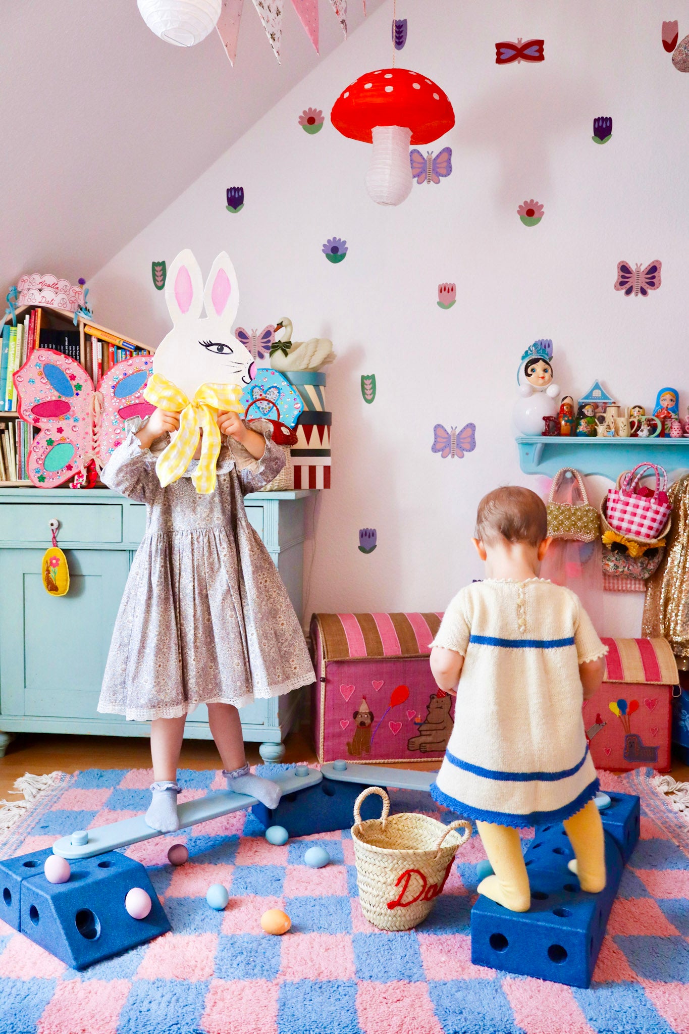 Two children playing in a colorful children's room with butterfly decals, toys and decorations.