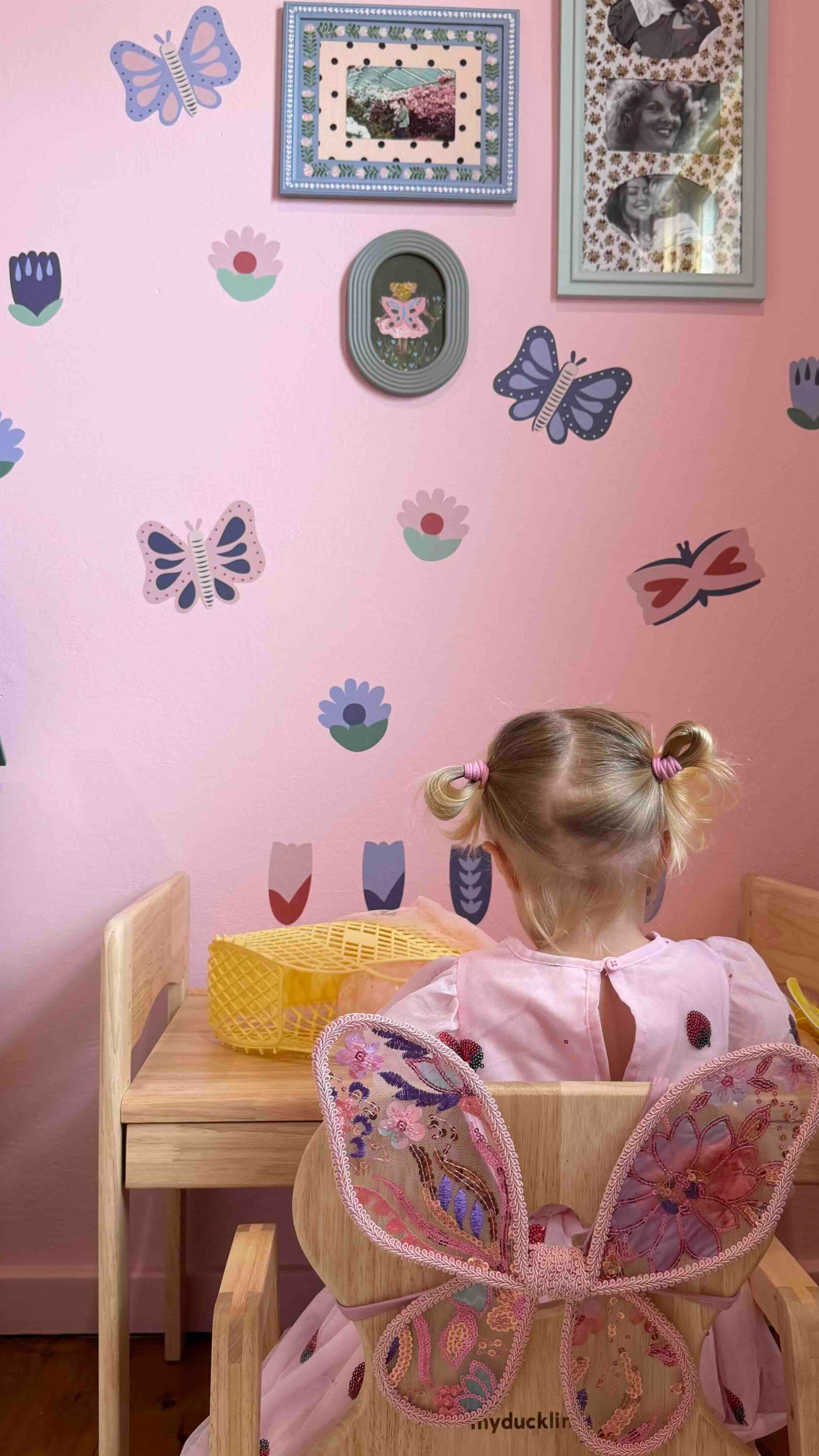 Child in a butterfly costume sitting on a chair in a room with pink walls and butterfly wall decals