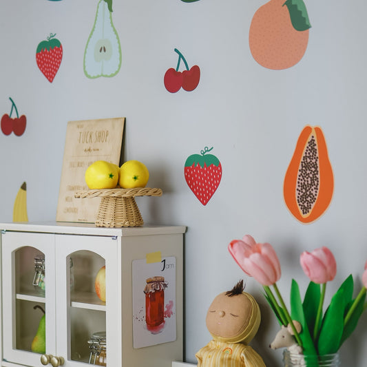 Children's play area with fruit-themed wall decals, a doll, and flowers.